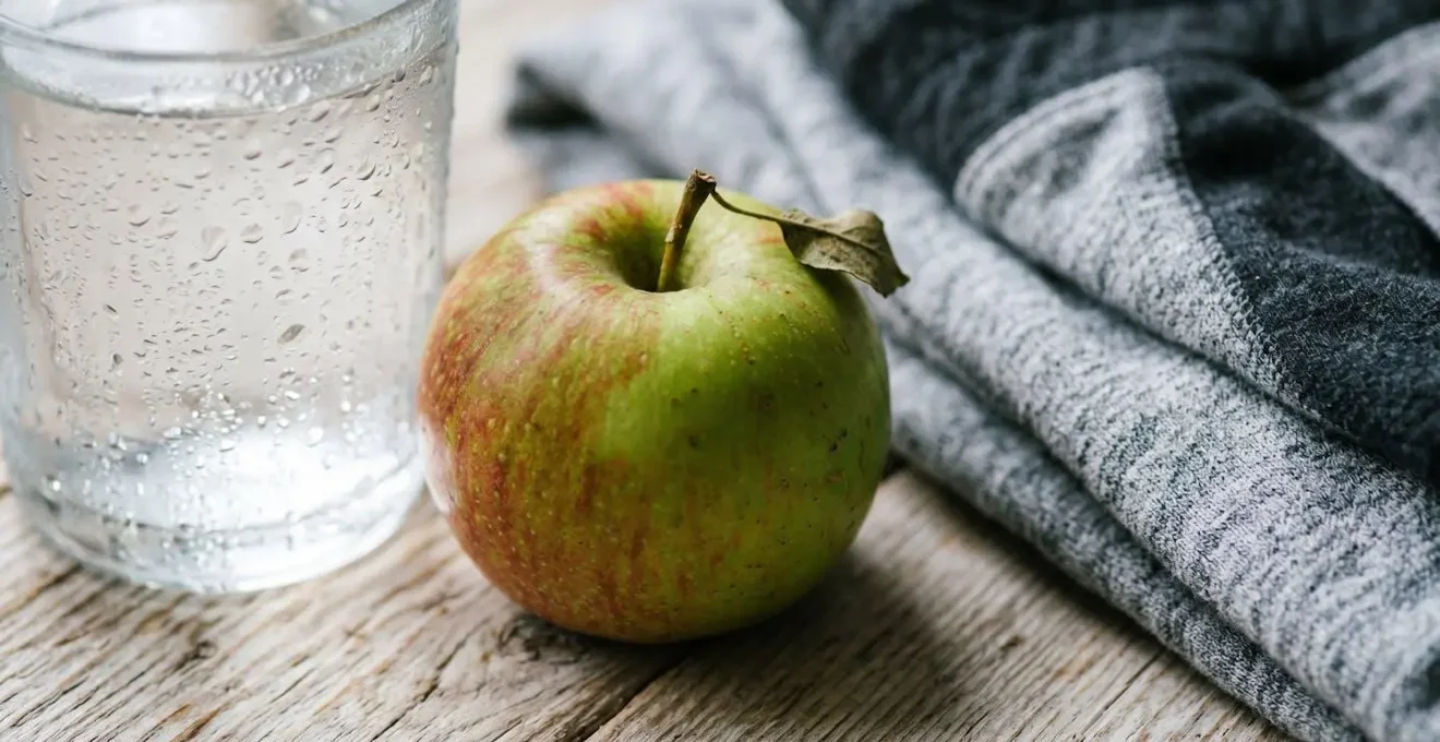 A minimalist arrangement of morning routine items: a glass of water, an apple, and folded workout clothes.