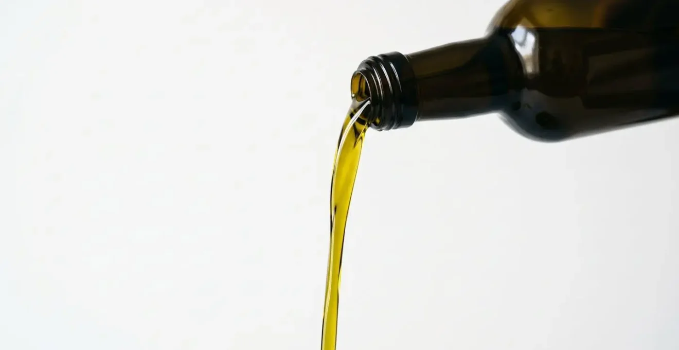 Golden extra virgin olive oil pouring from dark glass bottle with visible viscosity