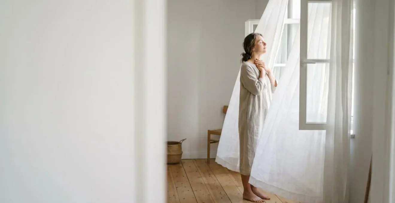 A person in a calm, sunlit room, practicing a vocal vibration technique to regulate their nervous system.